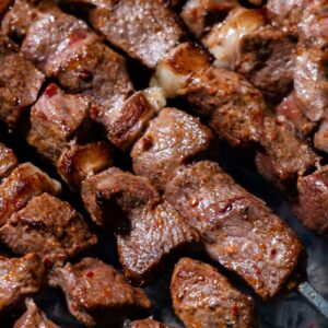 Close-up of deliciously grilled beef kebabs on skewers with a smoky background.